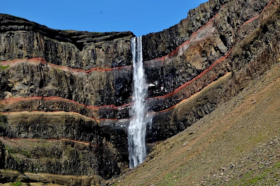 hengifoss waterfall pouring over vibrant red and black layered cliffs in iceland